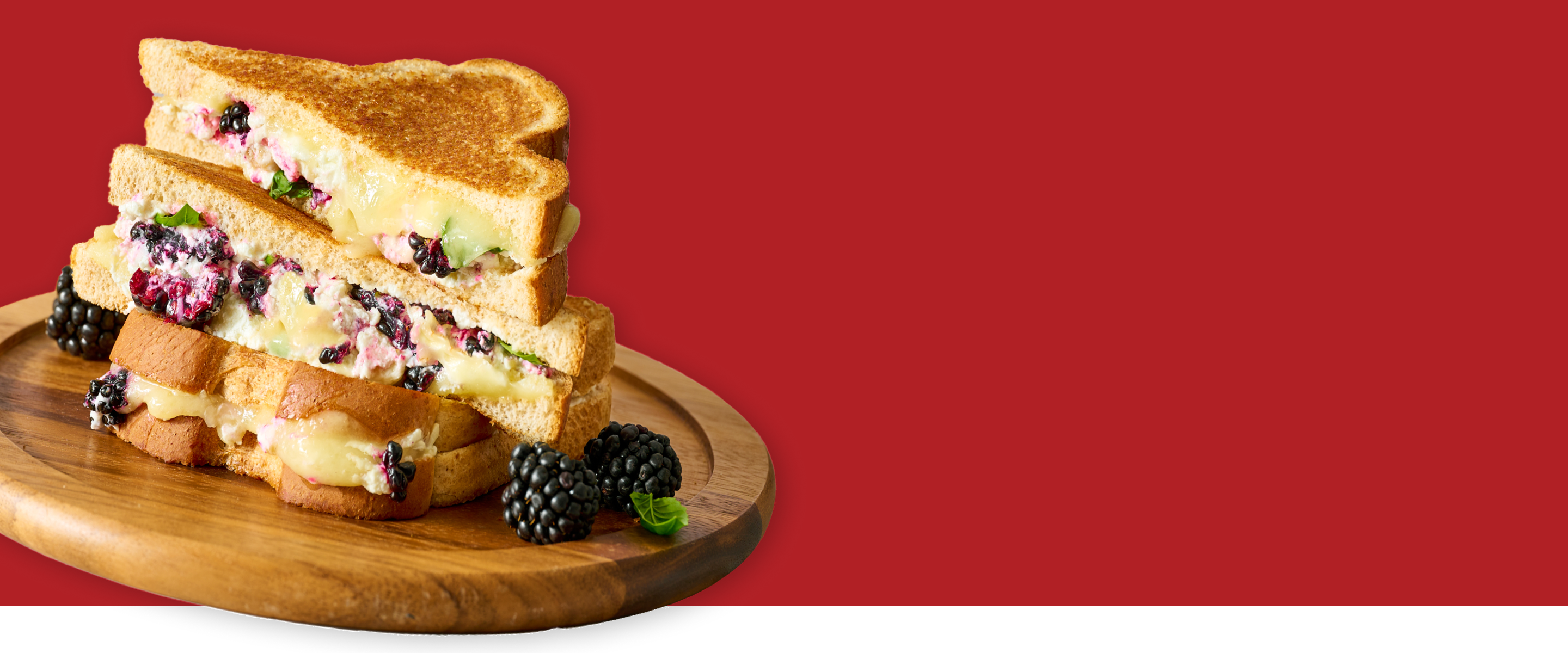 Stack of sandwiches with blackberries on a wooden board against a red background